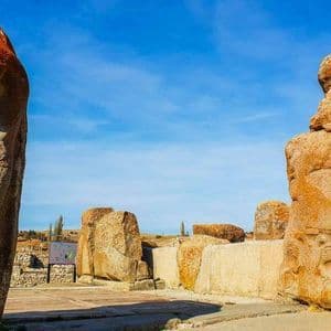 Due grandi monoliti in pietra con antiche incisioni, eretti in un sito archeologico sotto un cielo azzurro brillante.