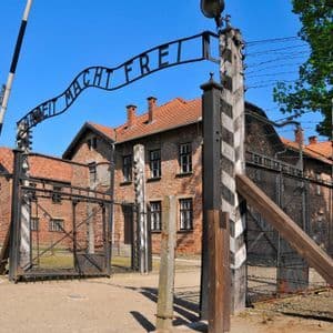 The entrance gate of the Auschwitz I concentration camp, with the sign 'Arbeit Macht Frei' above brick barracks and barbed wire fences.