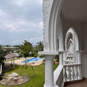 Una vista dal balcone di un resort attraverso una serie di archi bianchi, che si affaccia su un giardino con piscina.