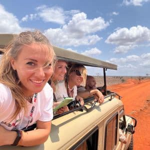 Un gruppo WeRoad scatta un selfie da un veicolo safari scoperto su una strada sterrata rossa nella savana.