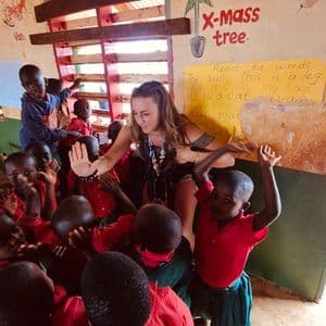 Una donna di un gruppo di viaggio WeRoad interagisce con un gruppo di giovani studenti sorridenti in un'aula con pareti dipinte.