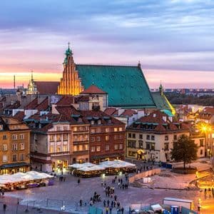 Una vista elevada de una plaza histórica de ciudad europea con edificios coloridos y una catedral, iluminada al atardecer.