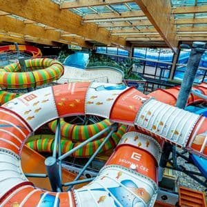 Blick von oben auf zahlreiche bunte, geschlossene Wasserrutschen, die sich durch einen Indoor-Wasserpark schlängeln.