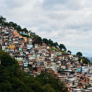Un ensemble dense de bâtiments colorés s'étend sur une colline luxuriante, sous un ciel nuageux.