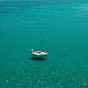 Una vista aerea di una barca a vela bianca che galleggia sola su un vasto, calmo mare turchese.
