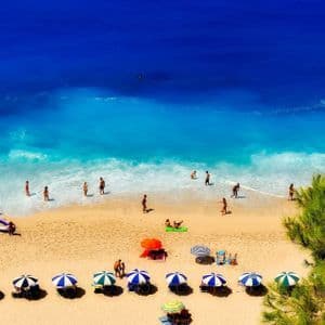 Una vista dall'alto di persone che si rilassano su una spiaggia sabbiosa con ombrelloni colorati vicino ad acque turchesi e blu profondo.