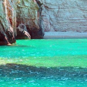 Acque turchesi e vibranti del mare incontrano la base di alte scogliere rocciose che costeggiano una spiaggia di ciottoli appartata.