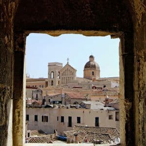 Un paisaje urbano soleado con tejados de terracota y una cúpula de iglesia, visto a través del marco de un arco de piedra.