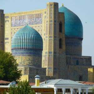 Un edificio sontuoso con grandi cupole turchesi e minareti decorati con intricati mosaici, sullo sfondo di un cielo limpido.