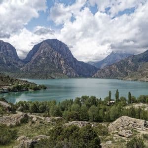 Un lago turchese si trova in una valle tra montagne rocciose, con un piccolo villaggio sulla riva sotto un cielo nuvoloso.