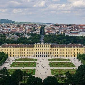 Una vista sopraelevata di un grande palazzo giallo con giardini all'italiana, sullo sfondo un'estesa città e colline.