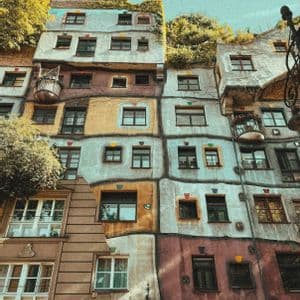 Una vista dal basso di un edificio multicolore con facciata irregolare, finestre non allineate e alberi sul tetto.