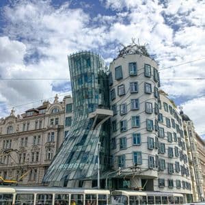 Un moderno edificio decostruttivista con una torre di vetro curva, con due tram rossi e bianchi che passano in primo piano.