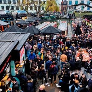 Una veduta dall'alto di una grande folla a un mercato alimentare all'aperto con bancarelle e tavoli vicino a un canale.