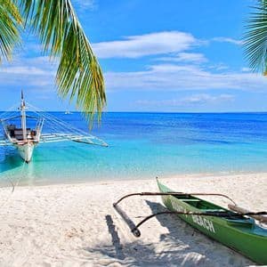 Dos barcas tradicionales en una playa de arena blanca con agua turquesa cristalina, enmarcadas por palmeras bajo un cielo azul.