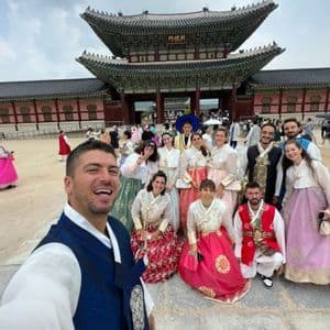 Un viaggio di gruppo WeRoad vestito in hanbok tradizionale coreano scatta un selfie nel cortile di un palazzo storico.