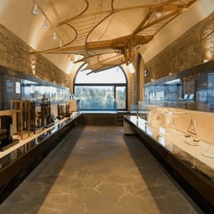Una sala espositiva di un museo con teche di invenzioni e un grande modello di macchina volante in legno sospeso dal soffitto a volta.