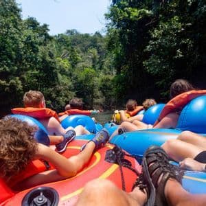 Un voyage de groupe WeRoad en gilet de sauvetage, descendant une rivière en bouée à travers une jungle luxuriante et verte.