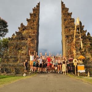 Un viaggio di gruppo WeRoad salta gioiosamente per una foto davanti a un grande, antico portale di pietra spaccata.