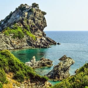 Una piccola cappella arroccata su un isolotto roccioso circondata da un mare turchese, con rigogliose scogliere verdi in primo piano.