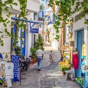 Un uomo anziano e un bambino piccolo percorrono una stretta via di ciottoli fiancheggiata da negozi ed edifici imbiancati a calce.