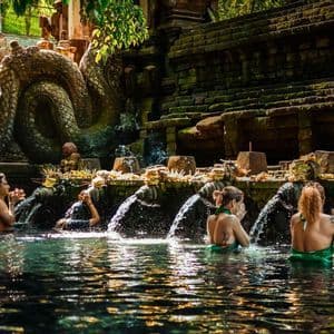 Un viaggio di gruppo WeRoad esegue un rituale di purificazione dell'acqua, lavandosi sotto le bocche di pietra di un tempio.