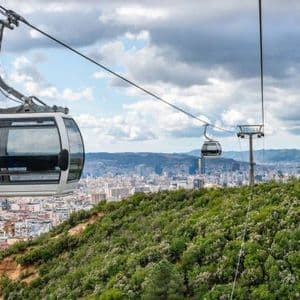Una moderna gondola di funivia si muove lungo una linea sopra una verde collina, con una città estesa visibile sullo sfondo.