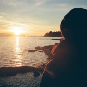 Une silhouette contemple le coucher de soleil se reflétant sur l'eau depuis une côte rocheuse.