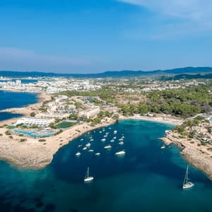 Vista aerea di una città costiera con una baia piena di barche e yacht ancorati sotto un cielo azzurro e limpido.