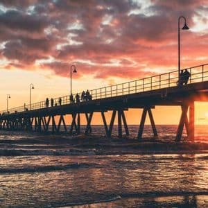 Siluetas de personas en un largo muelle sobre el océano durante un atardecer dramático y colorido.