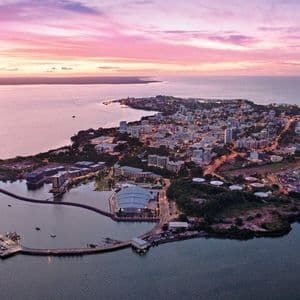 Una vista aérea de una ciudad costera con un gran puerto, iluminada por los tonos rosados y morados del atardecer.