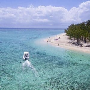 Vue aérienne d'un bateau à moteur blanc naviguant dans des eaux turquoises peu profondes près d'une plage de sable blanc avec des arbres.