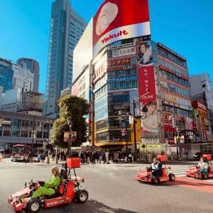 Un viaggio di gruppo WeRoad con go-kart rossi attraversa un affollato incrocio cittadino fiancheggiato da alti edifici moderni e cartelloni pubblicitari.