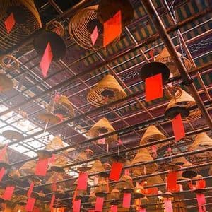 Una vista dal basso di numerose spirali di incenso coniche con etichette rosse, appese a un soffitto a griglia di legno.