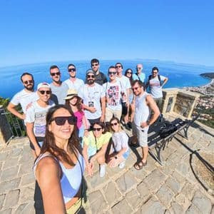 Un viaggio di gruppo WeRoad si scatta un selfie grandangolare su un punto panoramico che si affaccia su una città costiera e il mare blu.