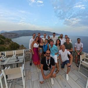 Un viaggio di gruppo WeRoad sorride per una foto su una terrazza con vista mare e una costa rocciosa.
