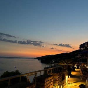 Una vista da una terrazza in pietra illuminata con affaccio sul mare e sulla costa in silhouette al tramonto.