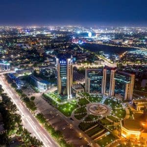 Una veduta aerea notturna di una città moderna, con grattacieli illuminati, un parco centrale e scie luminose del traffico stradale.