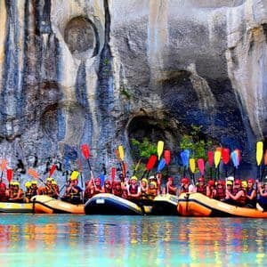 Un viaje en grupo de WeRoad levanta remos coloridos de sus balsas en un río tranquilo junto a una imponente pared de roca.
