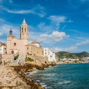Una grande chiesa con un campanile sorge su una costa rocciosa accanto al mare blu sotto un cielo parzialmente nuvoloso