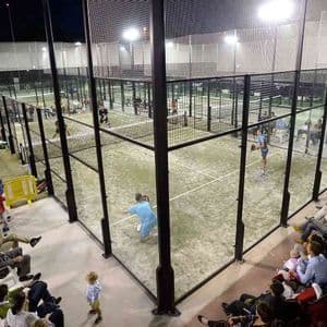Si gioca una partita di padel su un campo illuminato di notte, con spettatori a bordo campo.