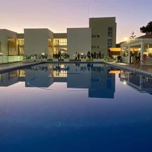 Una piscina riflette un edificio moderno e le luci al calar della sera, con un gruppo WeRoad riunito sul bordo piscina.