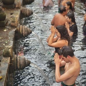 Un hombre y una mujer de un viaje en grupo de WeRoad rezando con las manos juntas bajo chorros de agua que fluye en una piscina de piedra.