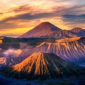 Un paisaje de cráteres volcánicos y montañas iluminado por un amanecer dorado, con humo saliendo de un cráter.