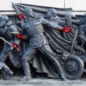 Un monumento di guerra in metallo scuro raffigurante soldati in combattimento, dove le loro mani e armi sono state dipinte di rosso vivo.