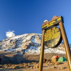 Le panneau du camp Karanga dans le parc national du Kilimandjaro, avec des tentes de camping et le sommet enneigé de la montagne en arrière-plan.