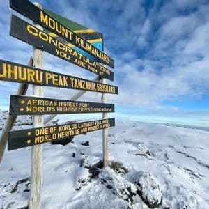 Le panneau en bois au pic Uhuru, le sommet du mont Kilimandjaro, se dressant dans un paysage enneigé sous un ciel nuageux.