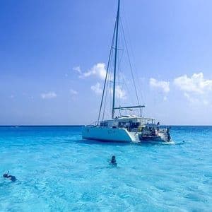 Eine WeRoad Gruppenreise beim Schnorcheln und Schwimmen im klaren türkisfarbenen Wasser neben einem Katamaran unter blauem Himmel.