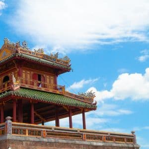 Un tradizionale edificio in stile asiatico con pilastri rossi, tetto di tegole verdi e dettagli ornamentali, su un cielo azzurro con nuvole.