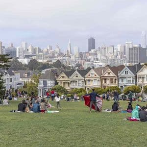 Un viaggio di gruppo WeRoad in relax su una collina erbosa, con vista su case vittoriane colorate e uno skyline cittadino sullo sfondo.